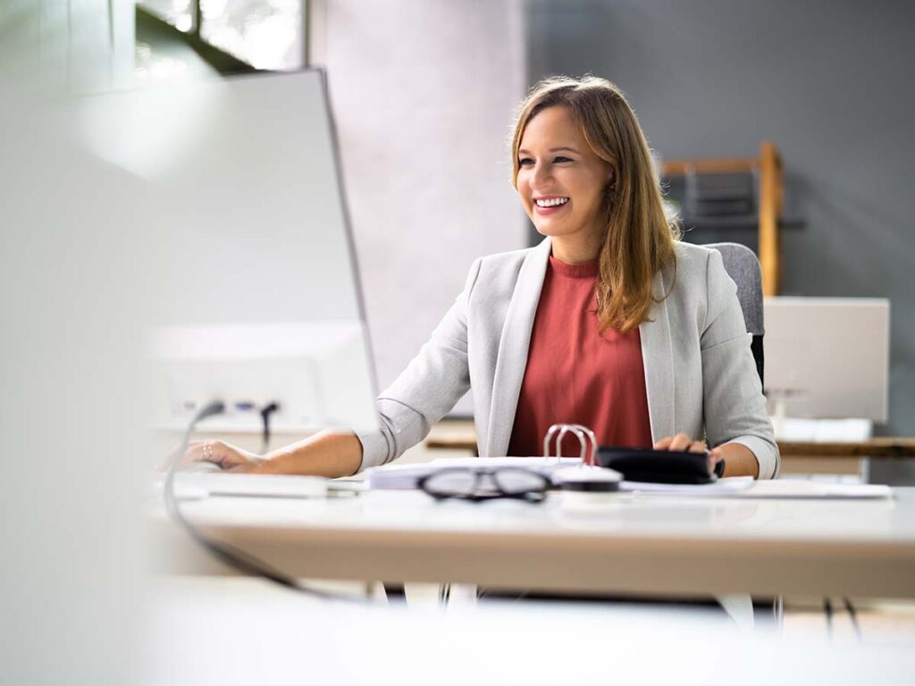 Frau im Büro am Computer, lächelnd und konzentriert. Moderne Arbeitsumgebung, effiziente Büroarbeit, Produktivität.