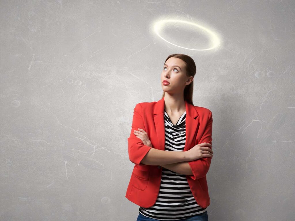 Frau in rotem Blazer mit Heiligenschein, nachdenklich blickend, steht vor grauer Wand. Konzept von Reinheit und Unschuld.