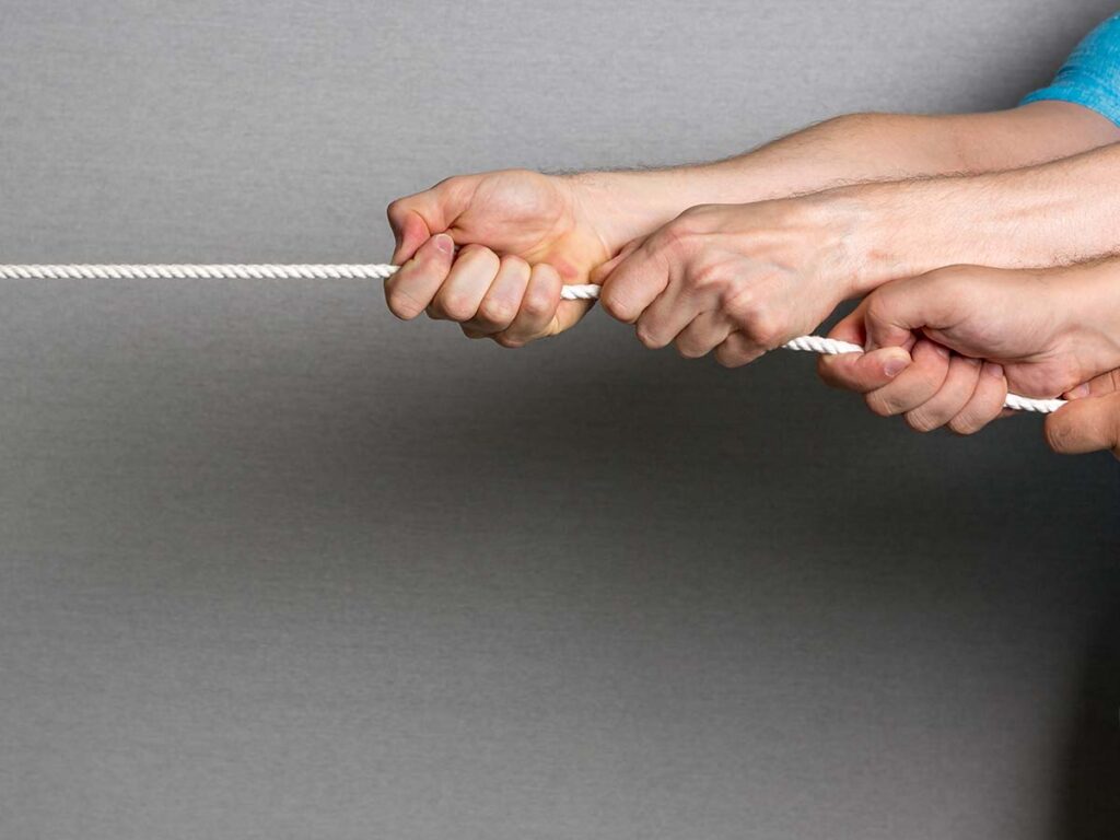 Menschen ziehen an einem Seil im Teamwork-Wettkampf, Konzept für Zusammenarbeit und Kraft, grauer Hintergrund.