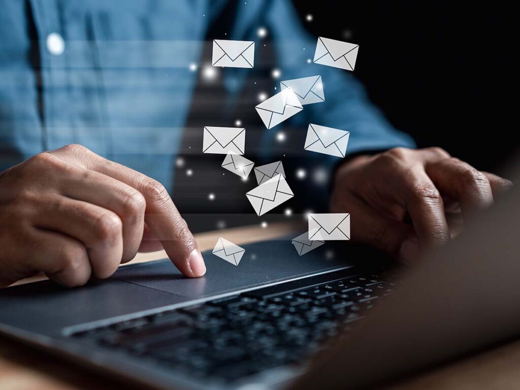 Person tippt auf Laptop, digitale E-Mail-Symbole fliegen heraus, Kommunikation, digitale Post, Technologie, Online-Nachrichten.