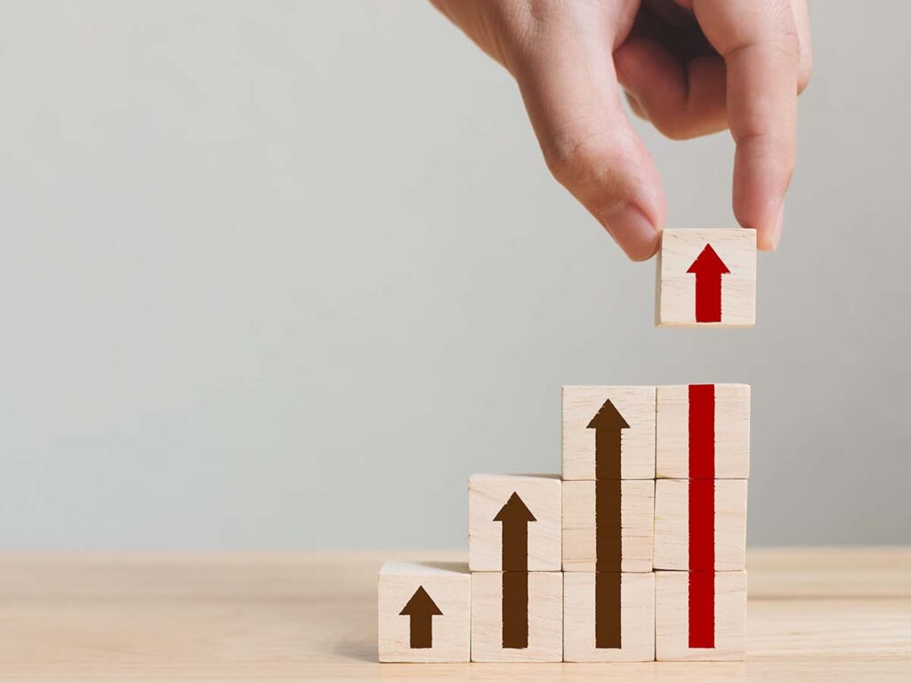 Wachstumskonzept dargestellt durch Hand, die Holzblock mit roten Pfeil auf steigende Pfeildiagramme platziert. Geschäftsstrategie.