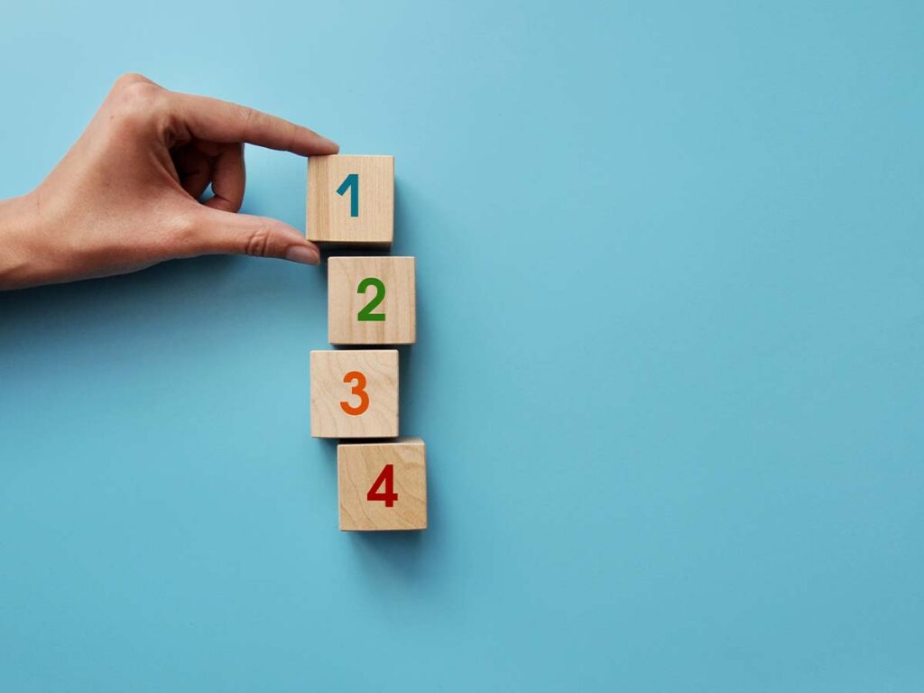 Hand ordnet nummerierte Holzblöcke 1 bis 4 auf blauem Hintergrund. Ideal für Themen wie Rangfolge und Organisation.