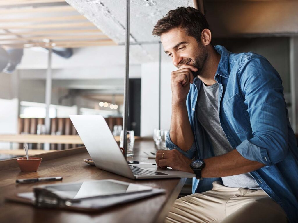 Mann in lässigem Outfit arbeitet konzentriert an Laptop in modernem Café. Freiberufler, Produktivität, digitales Arbeiten.