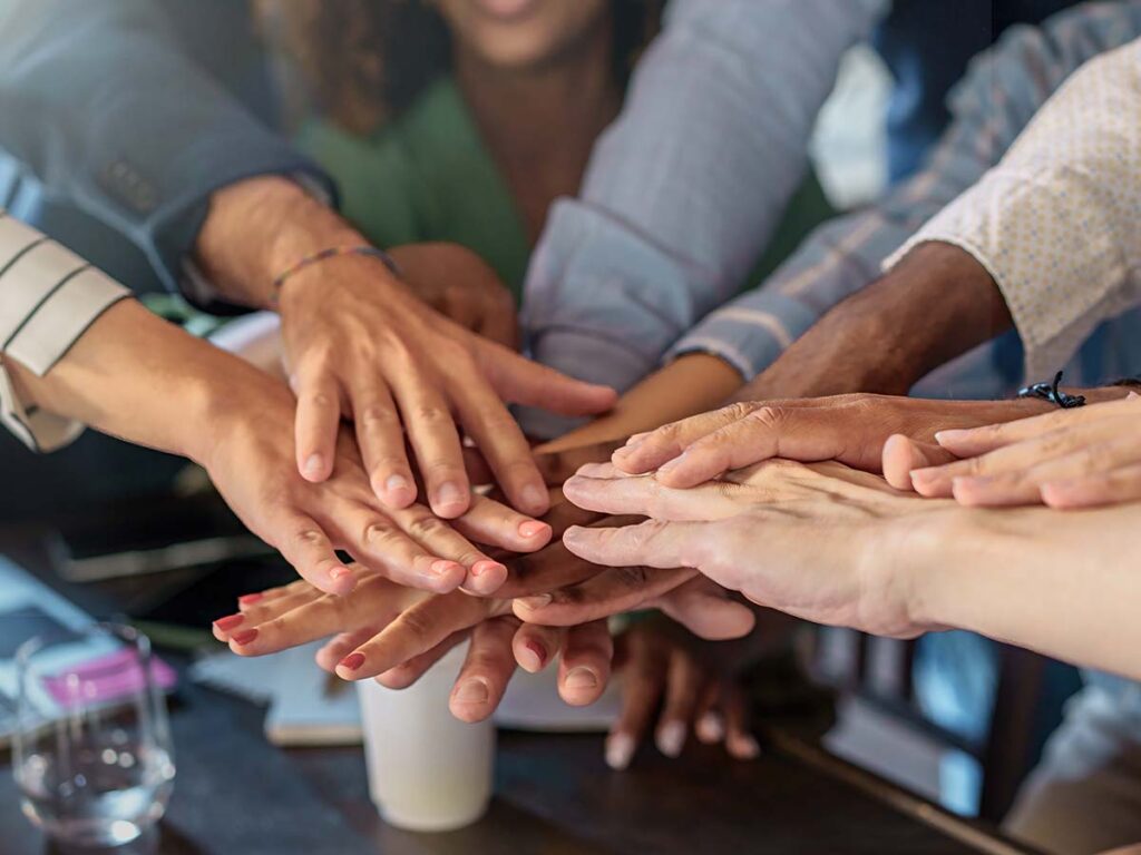 Verschiedene Hände in einem gemeinsamen Stapel symbolisieren Teamarbeit und Zusammenarbeit im Büro.