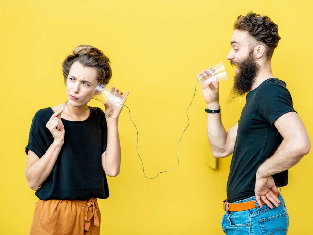 Zwei Menschen kommunizieren spielerisch über ein Schnurtelefon vor gelbem Hintergrund. Kreative Gesprächsmetapher.