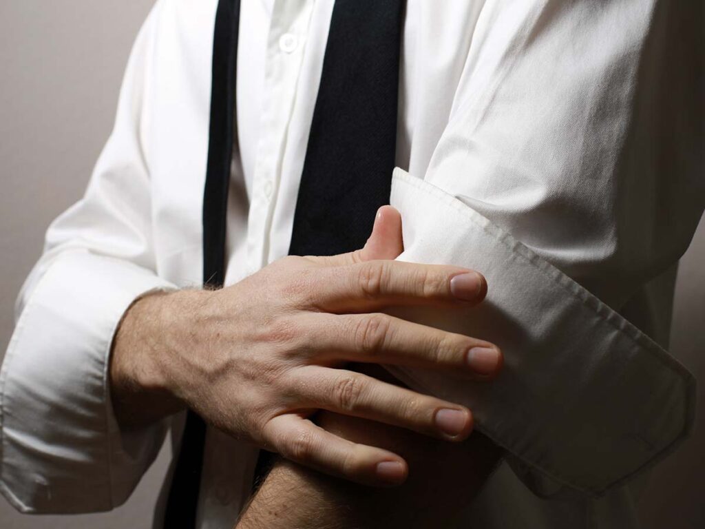 Mann rollt die Ärmel eines weißen Hemdes hoch, Business-Kleidung, Vorbereitung für Arbeit oder Meeting, seriöses Auftreten.