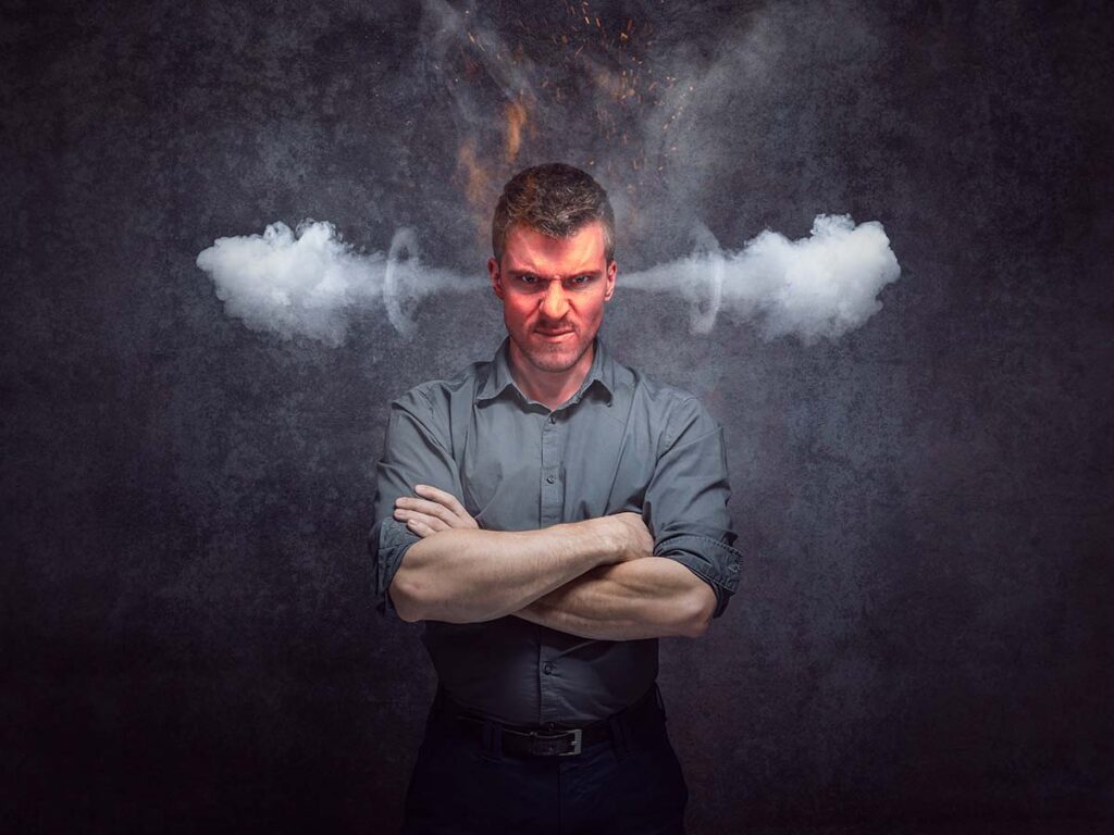 Wütender Mann mit verschränkten Armen, Dampf aus Ohren. Ausdruck von Frustration. Konzeptbild Emotionen und Stress.