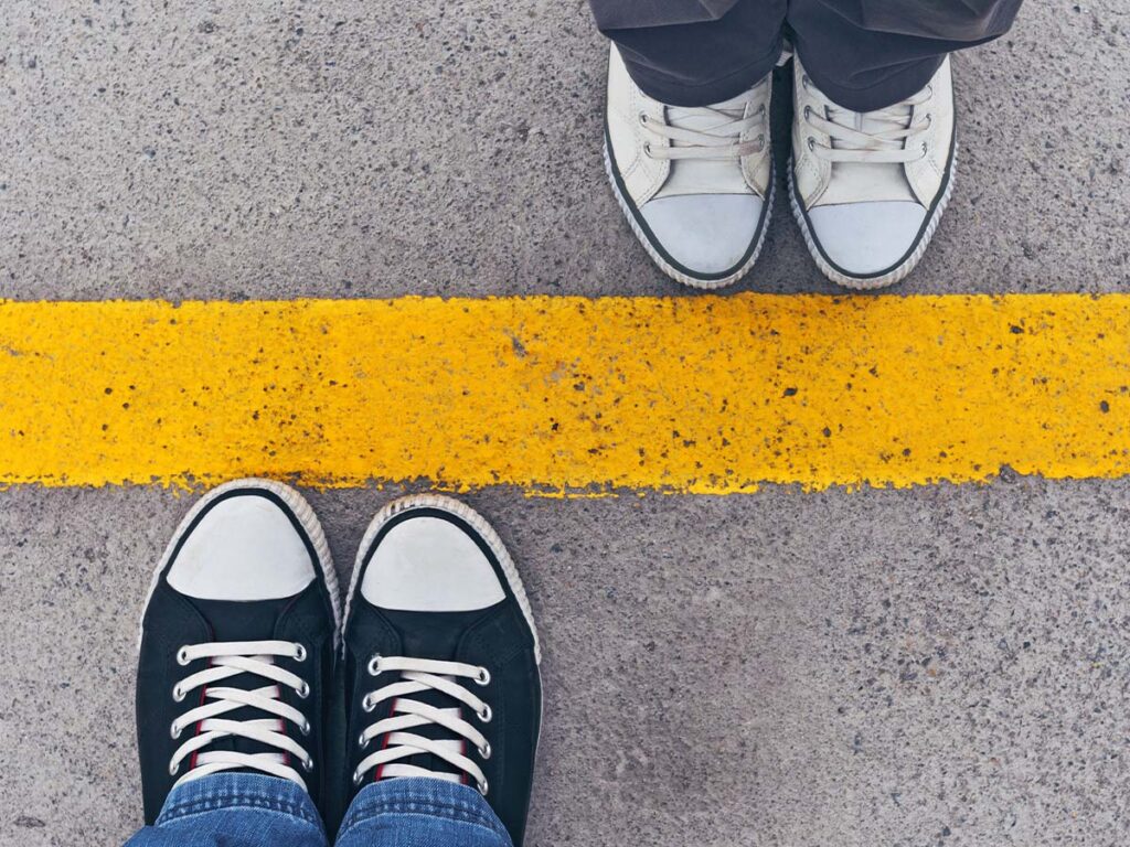 Schwarz-weiße Sneaker von zwei Personen stehen sich gegenüber, getrennt durch eine gelbe Linie auf Asphalt. Streetwear, Begegnung.