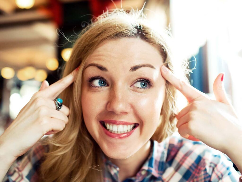 Lächelnde Frau zeigt auf ihren Kopf, trägt ein kariertes Hemd; Konzept für Freude und positive Gedanken.