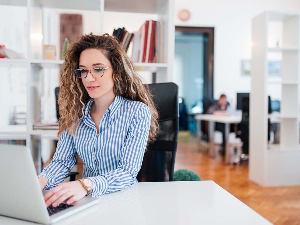 Frau mit Brille arbeitet konzentriert an Laptop im modernen Büro. Business-Frau, Arbeit, Produktivität, Büroumgebung.