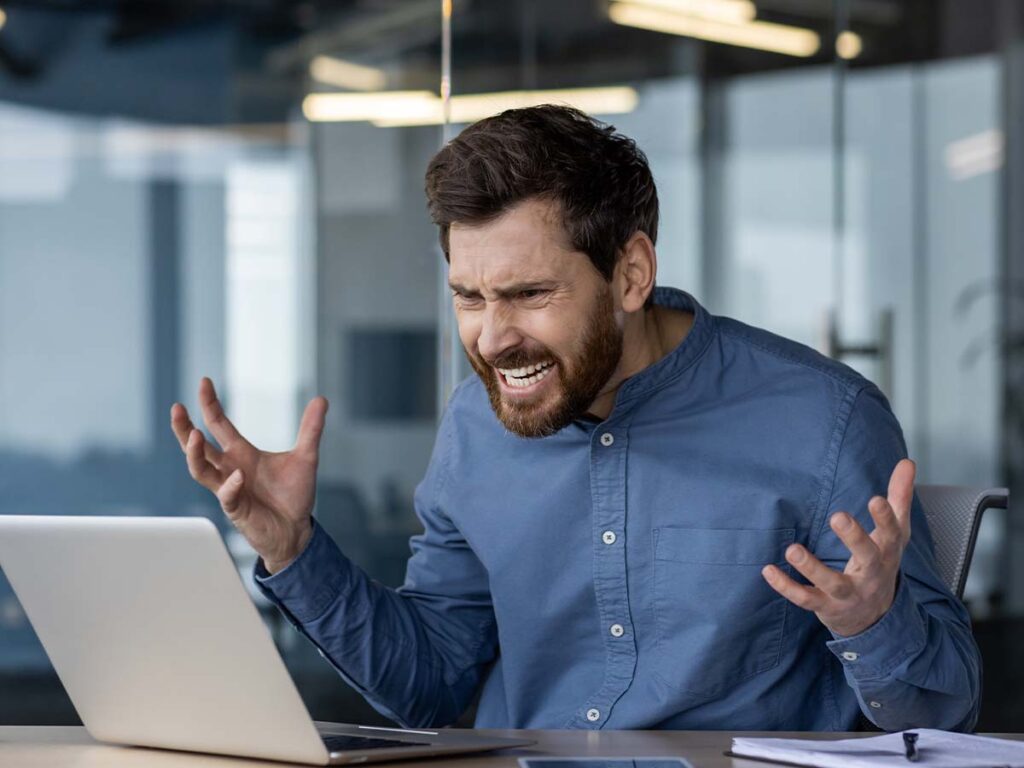 Mann frustriert am Laptop im Büro. Ausdruck von Stress bei der Computerarbeit. Job-Herausforderung, Technikproblem.