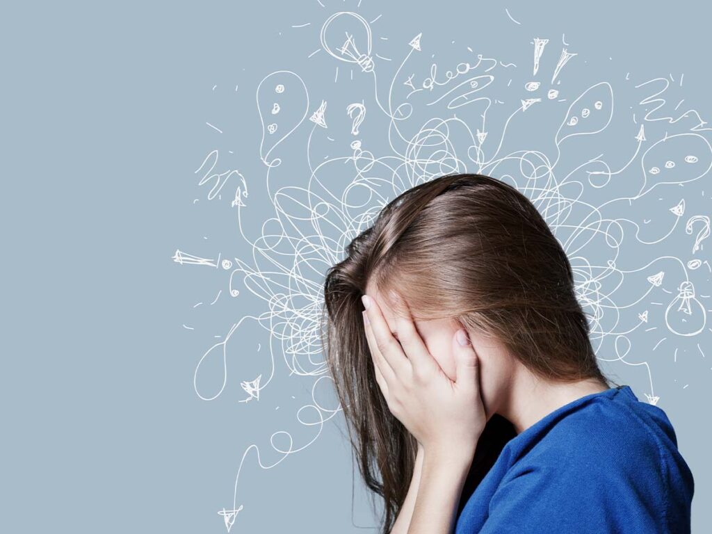 Gestresste Frau hält Gesicht in Händen, Symbol für Überforderung und Stress, mit verworrenen Kritzeleien im Hintergrund.