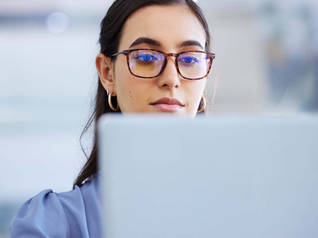 Eine Frau mit Brille arbeitet konzentriert am Laptop im Büro. Büroarbeit, Technologie und Produktivität.