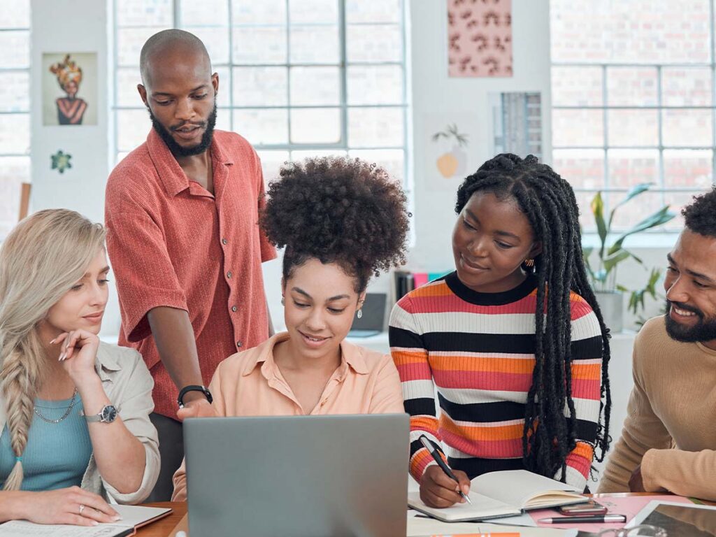 Teamarbeit im Büro: Fünf Personen diskutieren vor einem Laptop, planen Projekte, Zusammenarbeit, kreative Ideen, multikulturell.