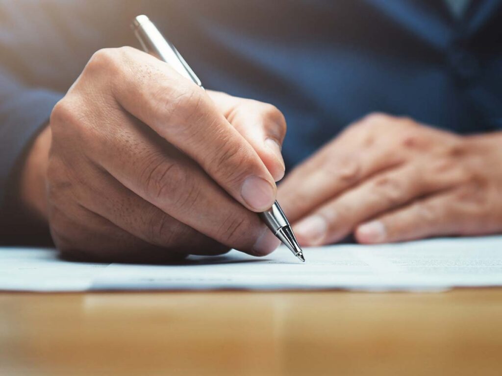 Ein Mann in Anzug schreibt mit einem silbernen Stift auf Papier.