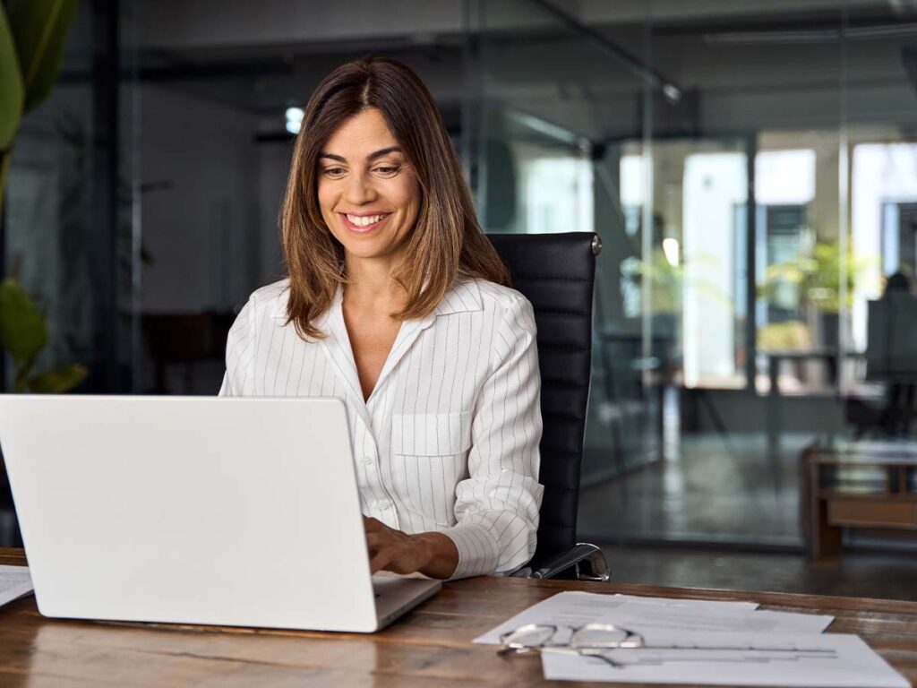 Frau im Büro am Laptop, lächelnd, arbeitet produktiv.