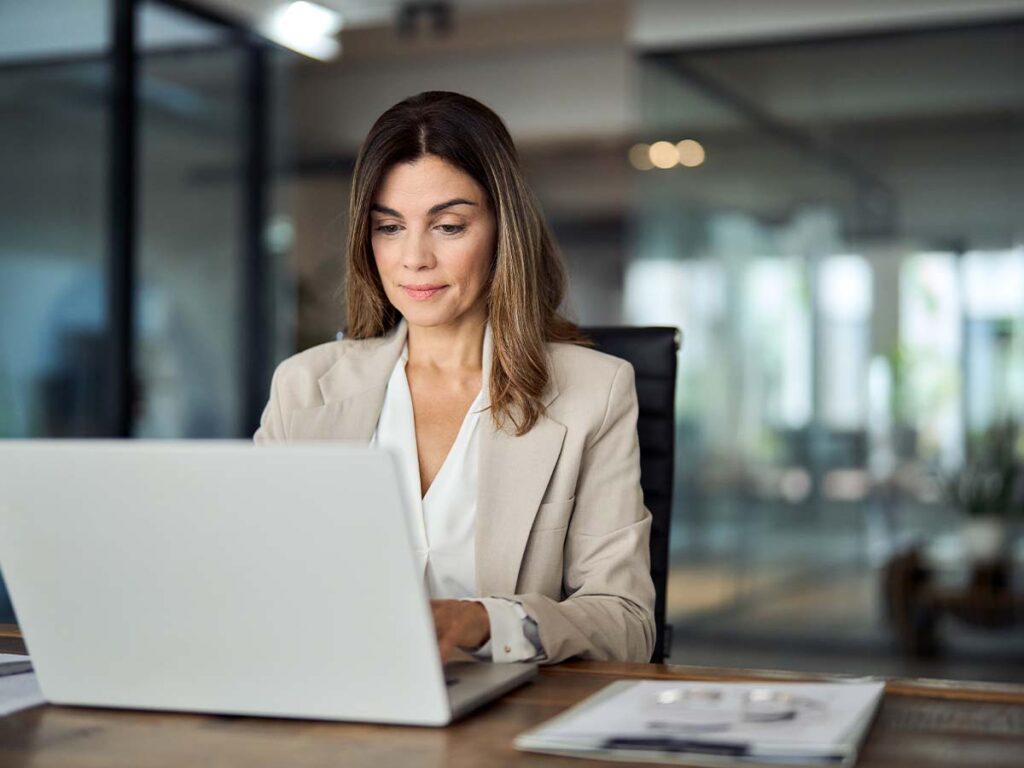 Eine Frau im Büro arbeitet konzentriert an einem Laptop. Kollegin-am-Laptop in moderner Arbeitsplatzumgebung.