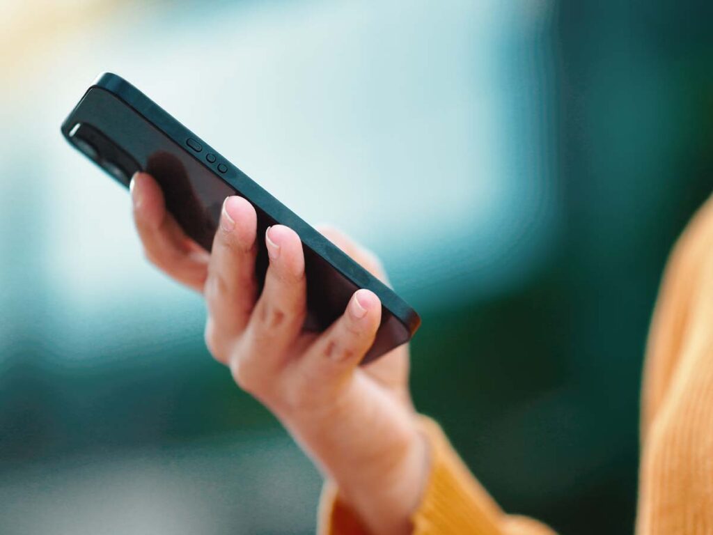 Eine Person hält ein Smartphone, Nutzung von Technik im Alltag, Nahaufnahme der Hand mit Handy, moderne Kommunikation.