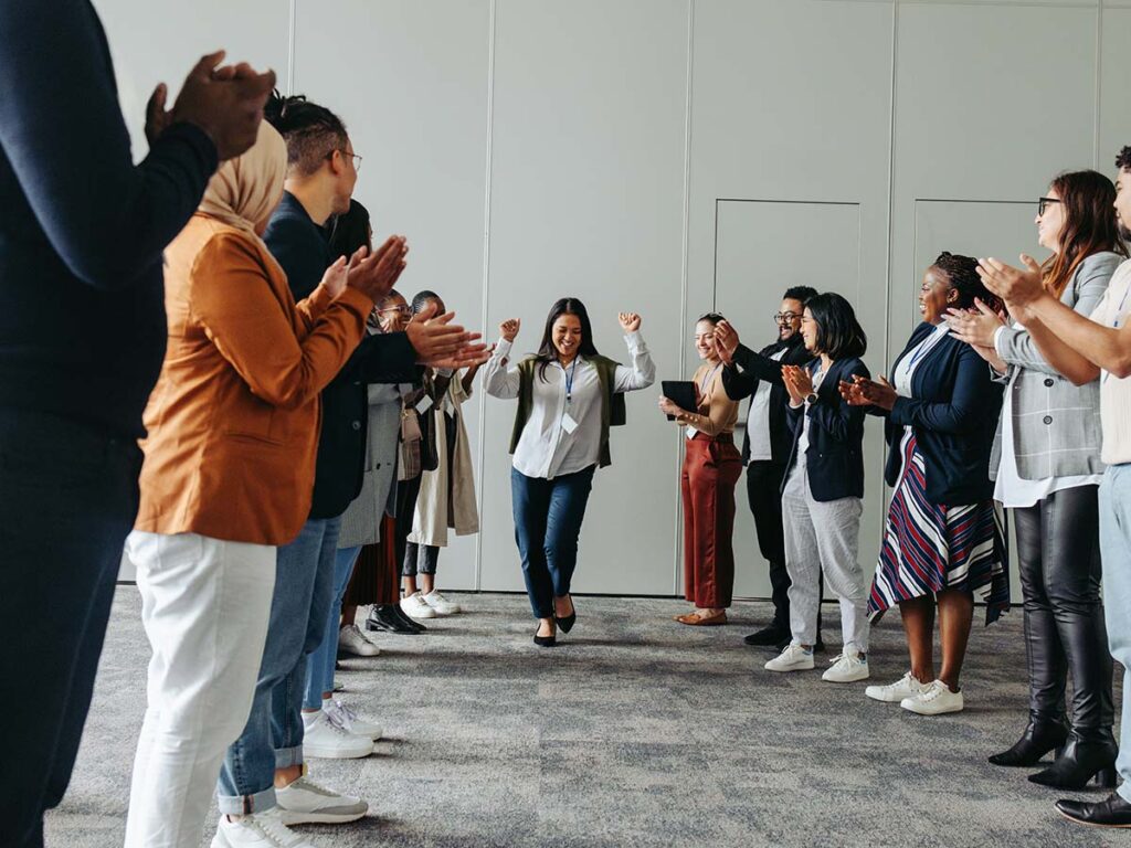 Person geht durch applaudierende Gruppe im Büro, Vielfalt, Erfolg und Teamwork hervorgehoben. Büroumgebung, Mitarbeiter.
