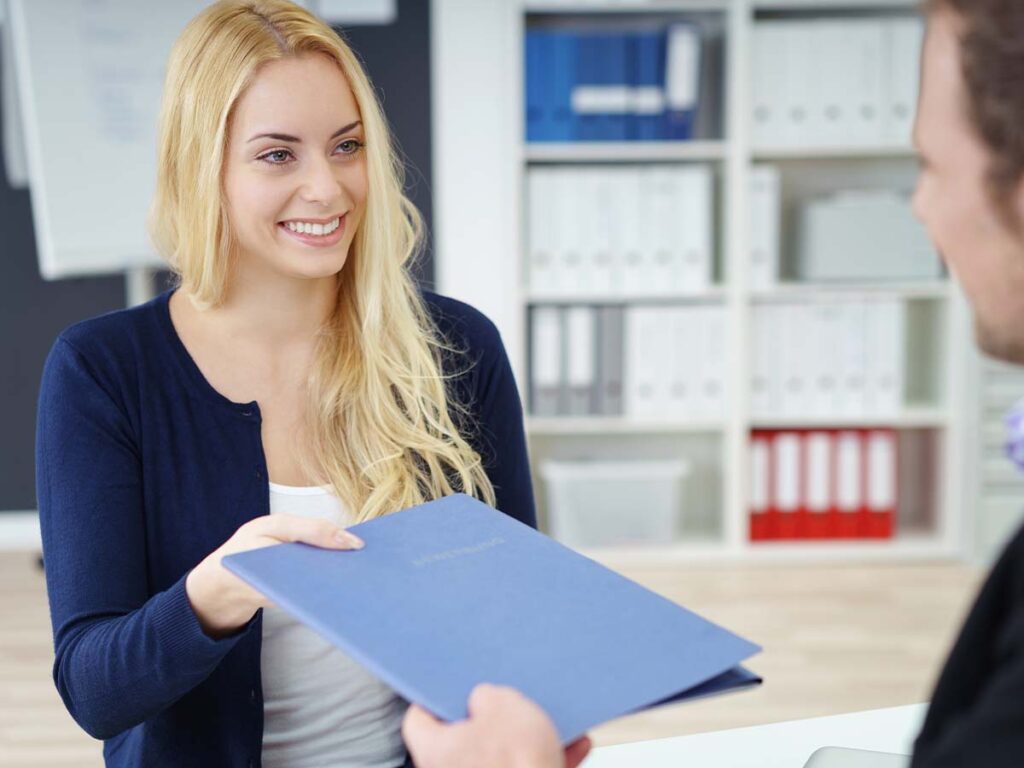 Eine Frau überreicht in einem Büro einem Mann eine Bewerbungsmappe. Geschäftstreffen, Bewerbung, Arbeitsplatz.