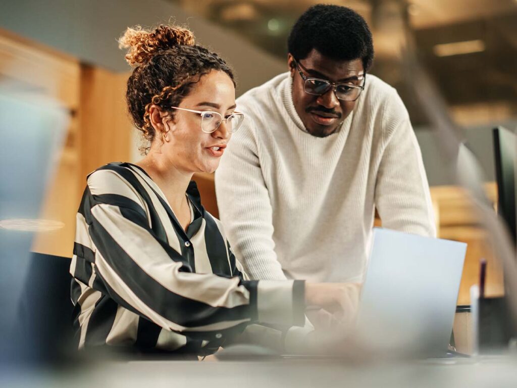 Das Bild zeigt zwei Kollegen, die an einem Laptop arbeiten.