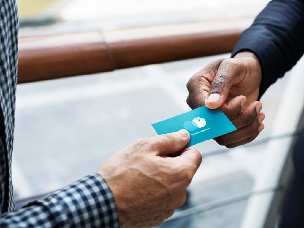 Zwei Personen tauschen Visitenkarte aus, symbolisiert Networking und Geschäftskommunikation. Fokus auf Hände und Karte.