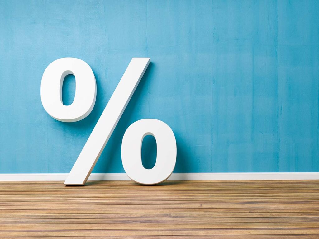 Weißes Prozentzeichen auf Holzboden vor blauer Wand. Symbol für Prozentsätze in Finanzen und Rabatten.
